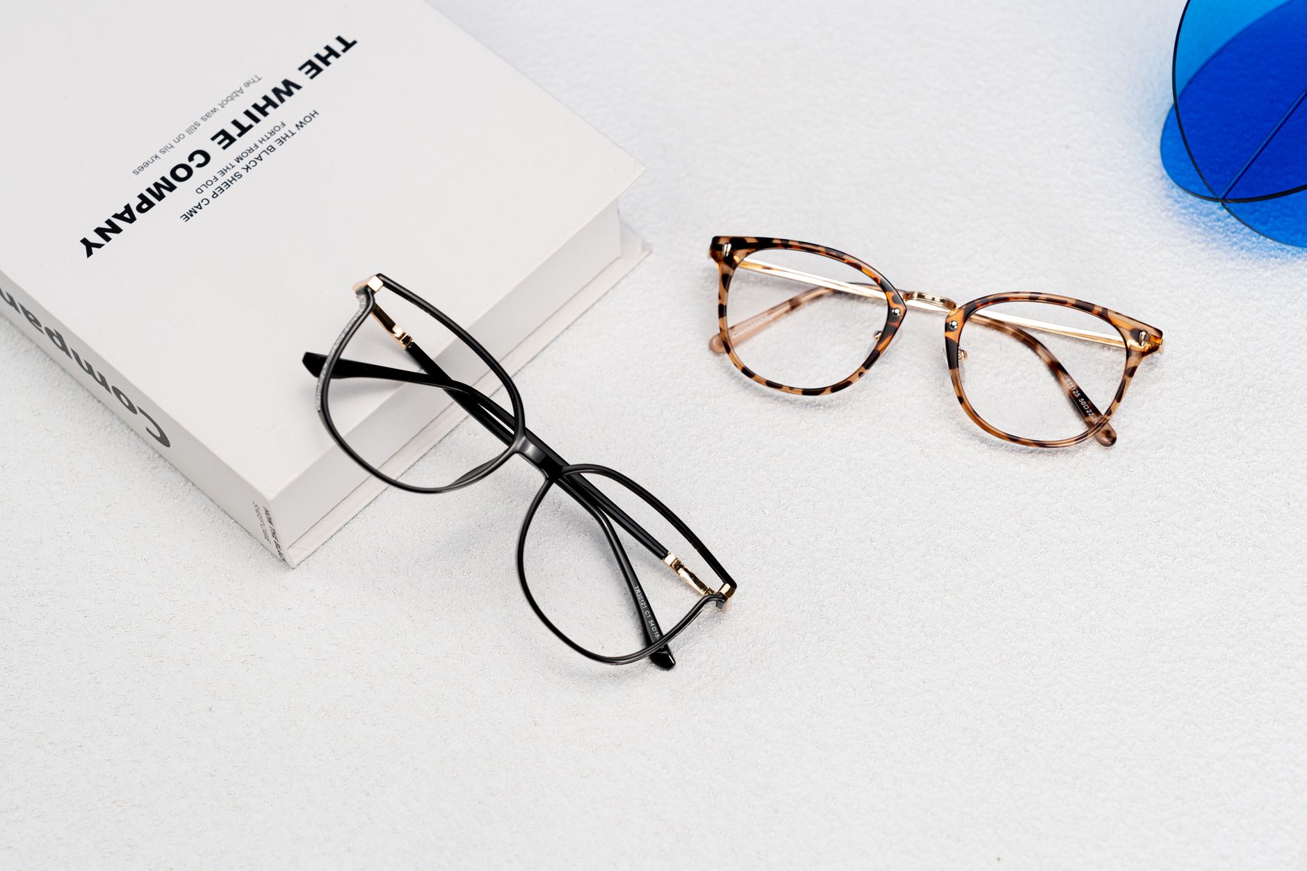 Elegant glasses beside a book on a minimalist surface, showcasing fashion and style.