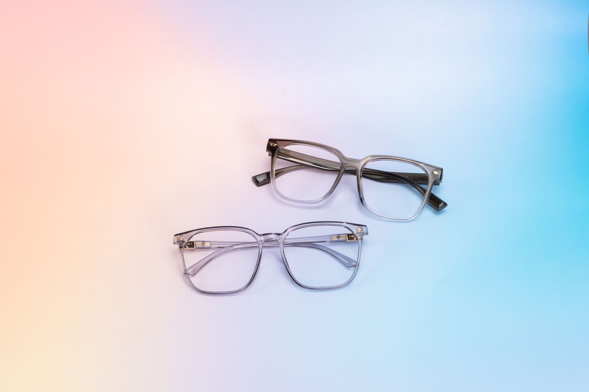 Two stylish pairs of eyeglasses on a gradient pastel background, highlighting eyewear design.