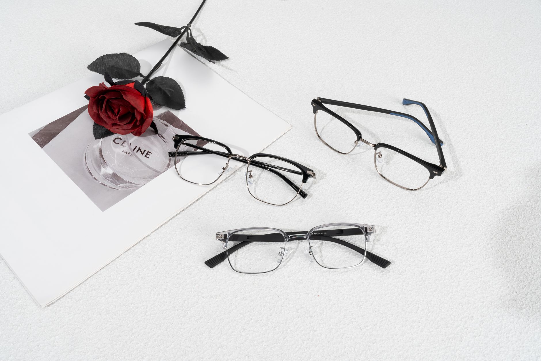 Modern eyewear arrangement with a red rose and stylish magazine backdrop.
