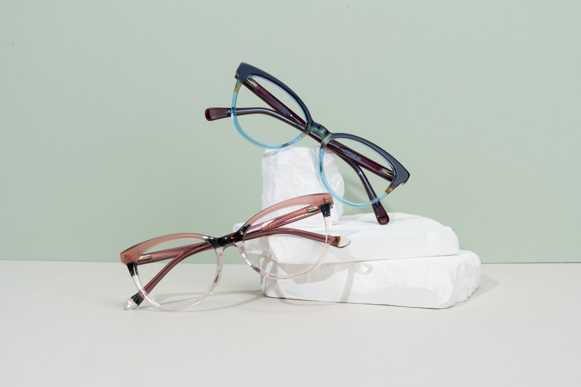 Modern eyeglasses with vibrant frames displayed on minimalist white pedestals.